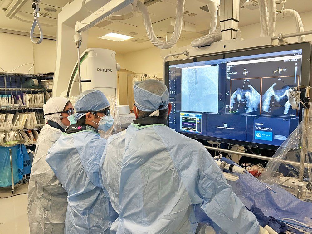 Surgeons perform a minimally invasive heart procedure. They look at echocardiograms on a large screen.