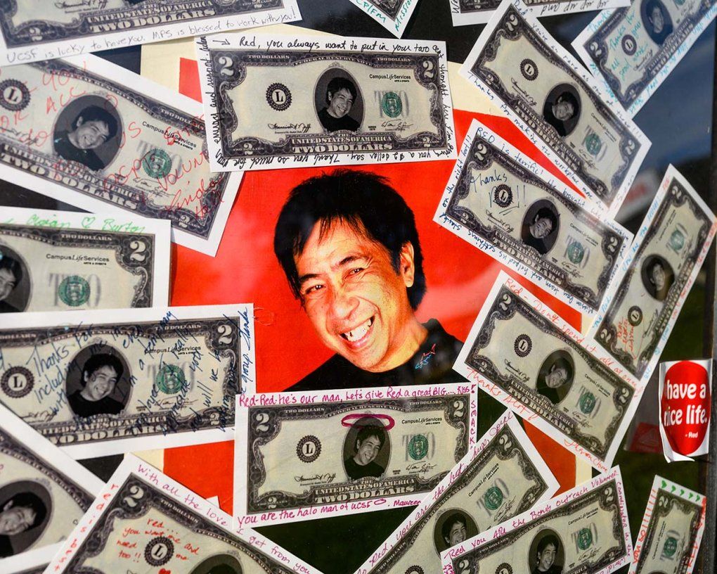 A memorial poster for Red Mangio with his face in the center and 2-dollar bills with personal notes taped around it.