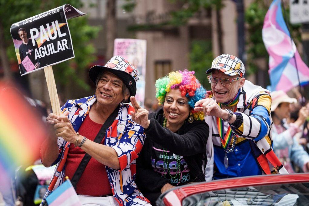Monica Gandhi wears a clown wig and waves to a spectator as she marches with two men during the SF Pride Parade.