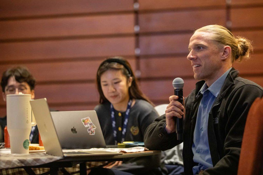 Brian Cairns speaks into a mic at an event with students.