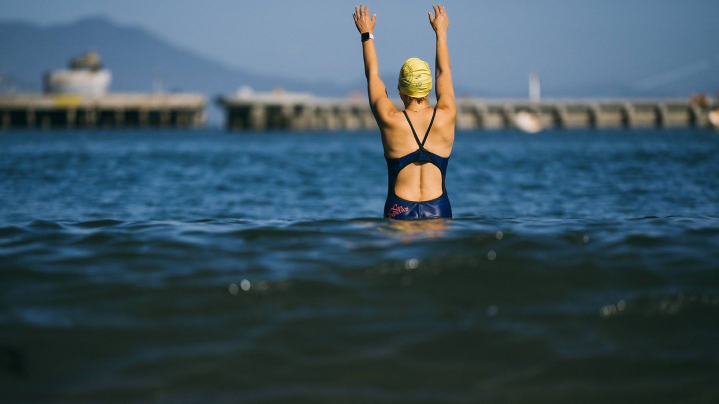 Angie Jacobson raises her arms above her head while she stands in the water of the bay, ready to dive in