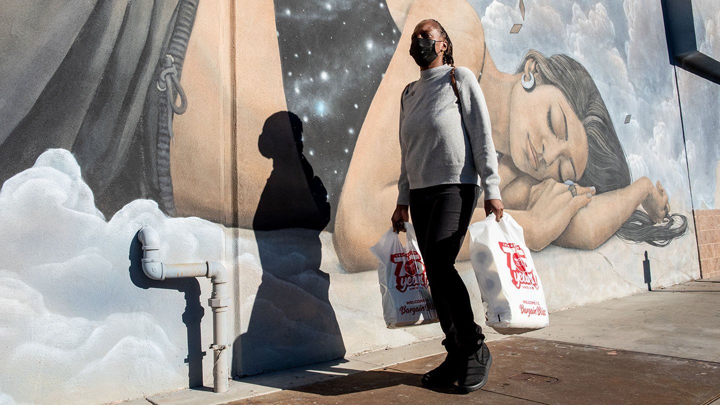 Rashetta Higgins walking past a mural of a woman dreaming with bags in her hands