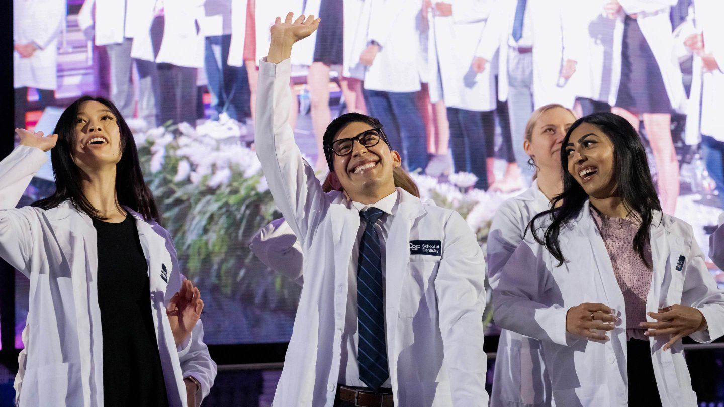 Students at white coat ceremony wave.