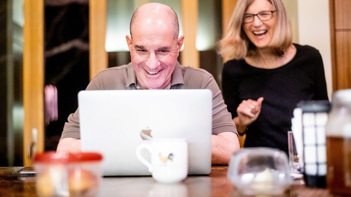 David Julius takes a call on his computer at home while his wife looks on and smiles