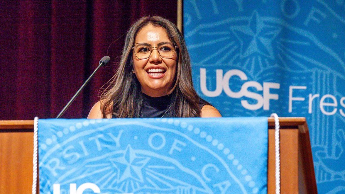 A woman smiles exuberantly at a podium with a backdrop reading UCSF Fresno behind her