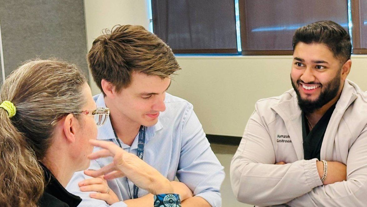 Man smiles at women across the table in a discussion.