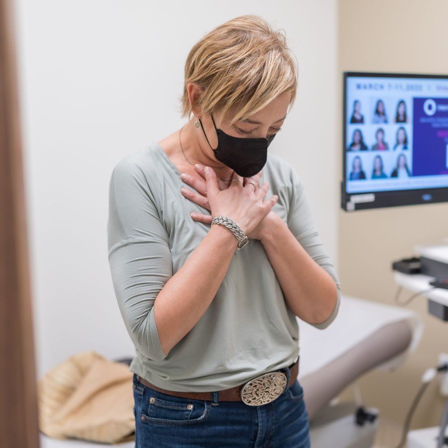 Angie Jacobson puts her hands to her heart and bows her head in an exam room