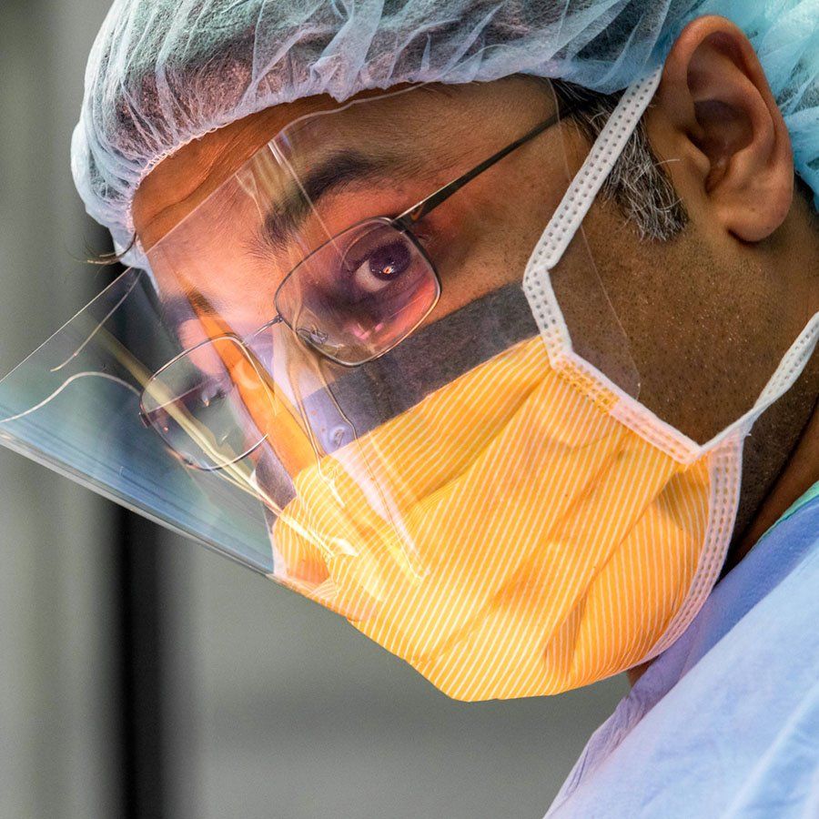 Praveen Mummaneni wears a surgical mask and face shield during an operation