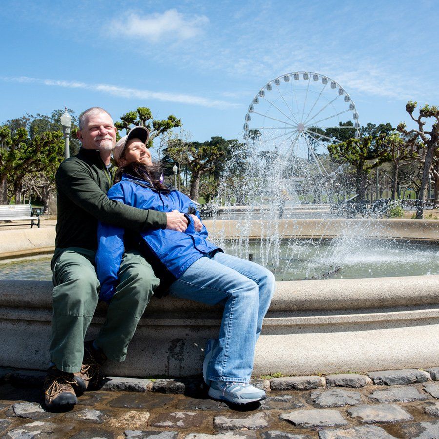 Cheryl and her partner embrace while sitting at the edge of a fountain in Golden Gate Park