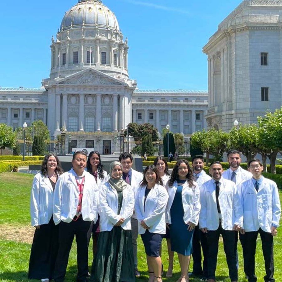 A group of medical students wearing white coats stand outside a state capitol building.