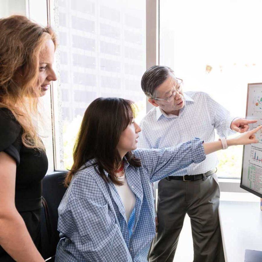 Reseracher Yaqiao Li shows a screen with scientific data to Marina Sirota and Yadong Huang in a sun-lit lab.