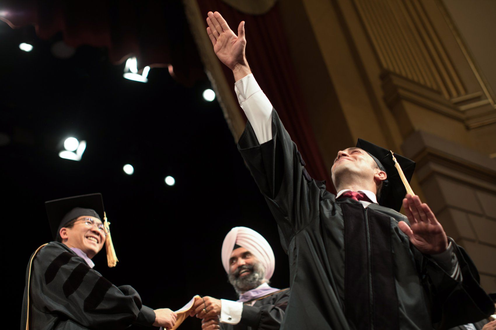 Student raises arm before receiving hood on stage