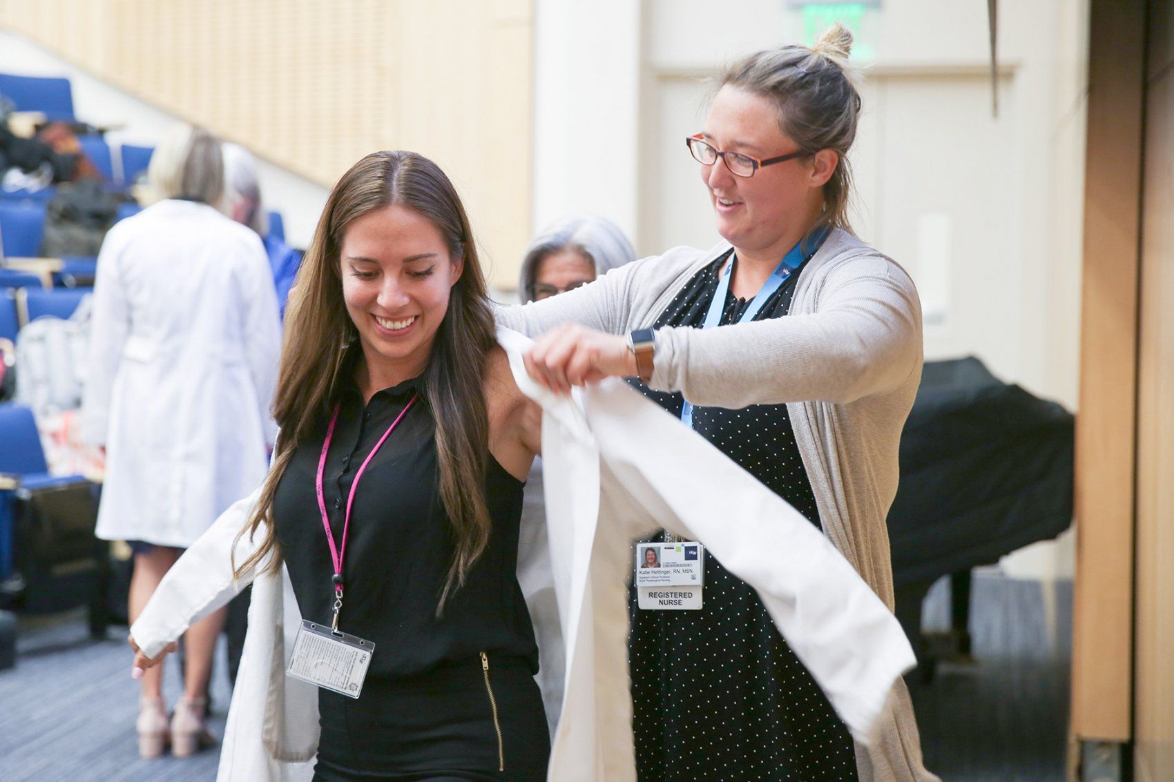 a woman slips a white coat onto a student