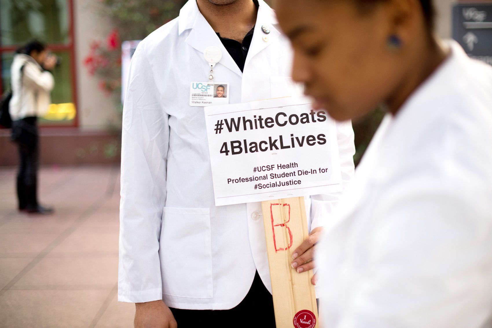 a student in a white coat holds a sign that says #WhiteCoats3BlackLives