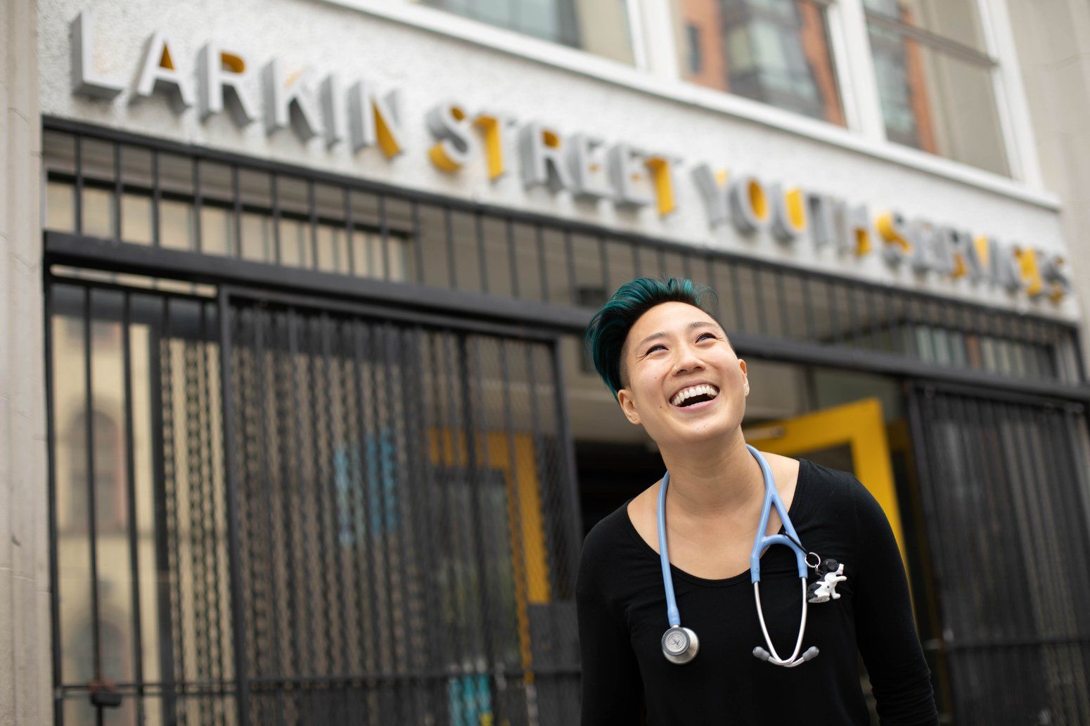 Woman wearing stethoscope laughing outside Larkin Street Youth Services