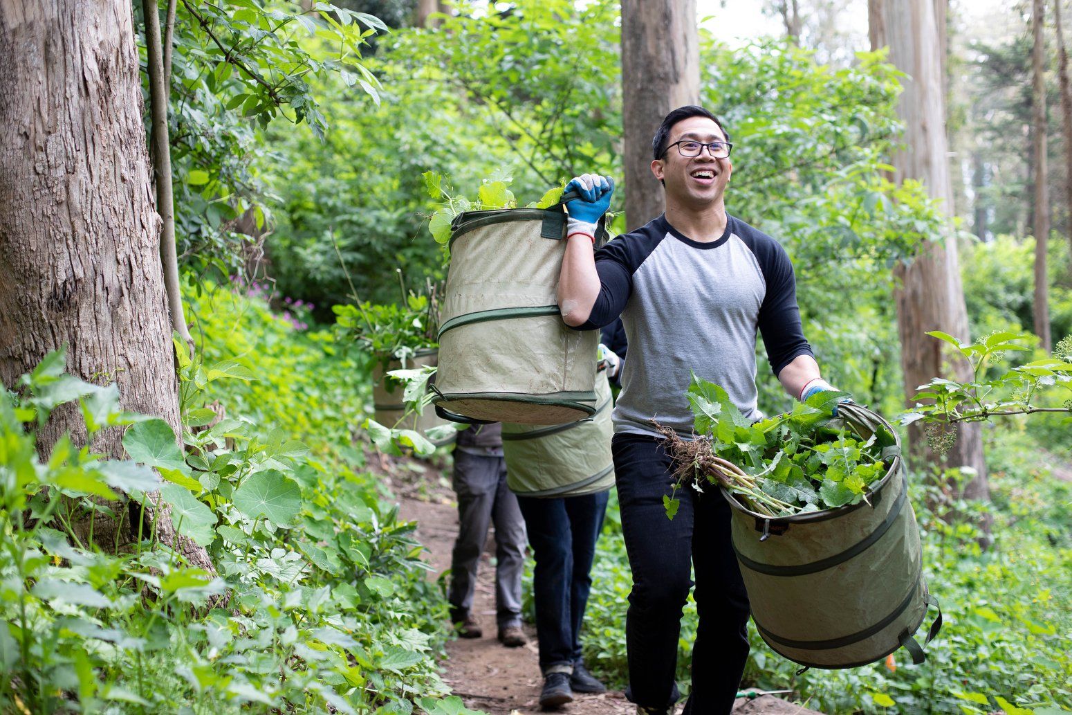 Three people carrying buckets of leaves outdoors