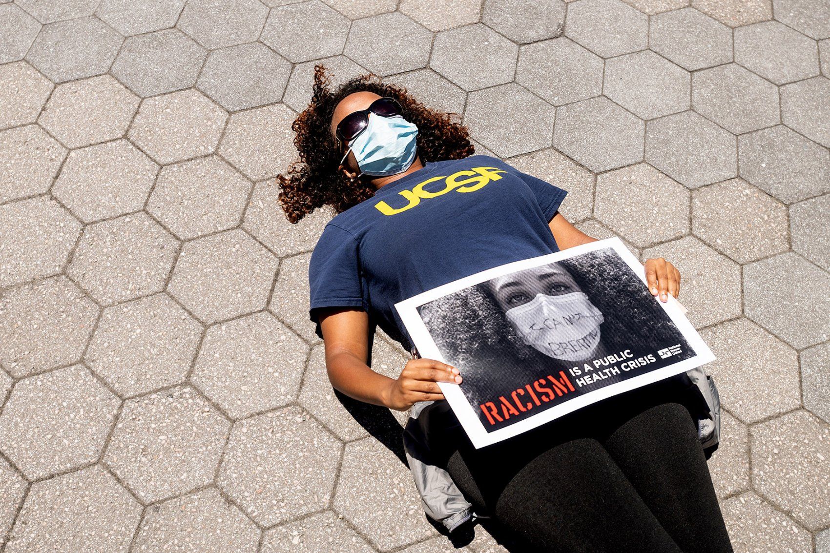 woman lies on the ground and holds a sign during a rally