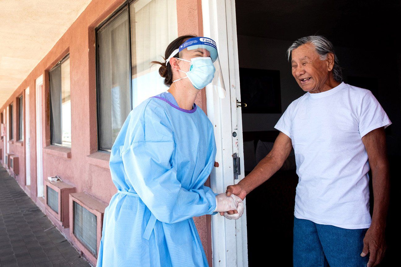 A UCSF resident shakes the hand and laughs with a Navajo resident quarantined in a motel in Gallup
