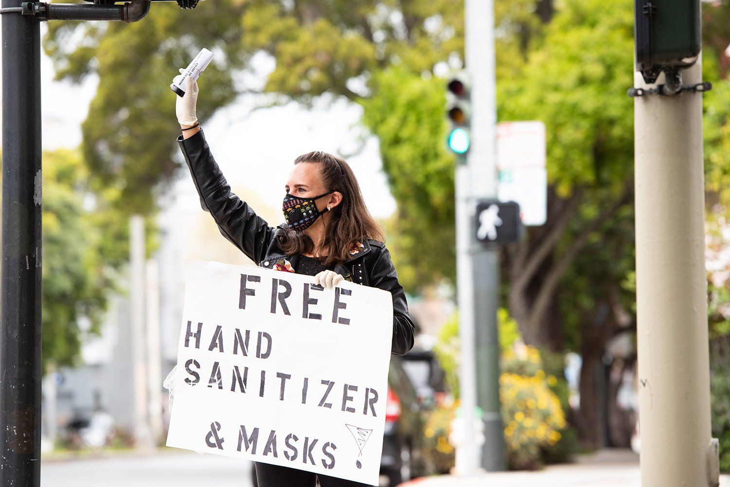 A UCSF postdoc holds up a sign that says free hand sanitizer and masks while holding a bottle of hand sanitizer up in her other hand