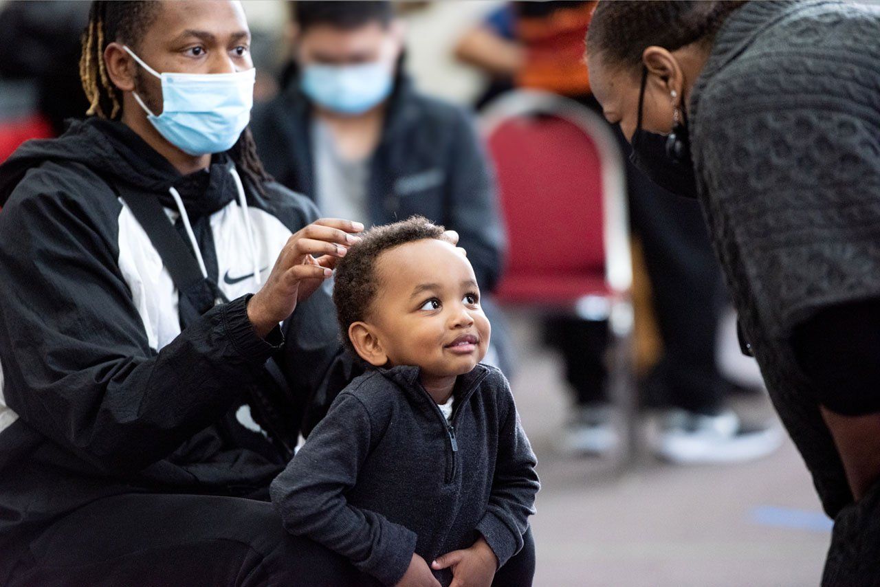 A little boy looks up at a vaccination center volunteer while his dad gently touches his head