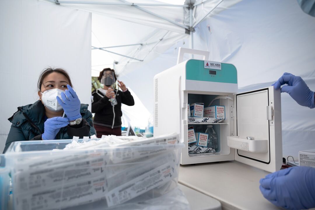Staff members prepare doses of the Moderna vaccine in a tent at a community pop-up vaccination site