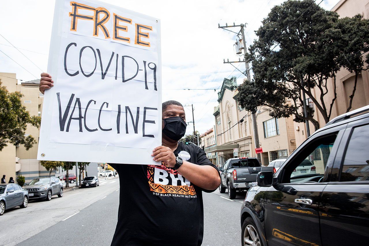A man walks along a street holding a sign that reads Free COVID-19 Vaccine