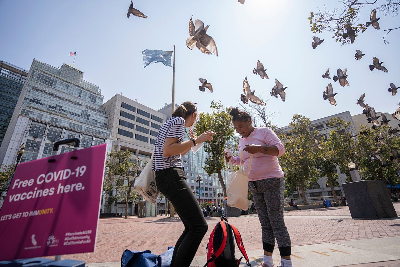 Pigeons fly up around two women, one who just received her vaccine and one who is volunteering