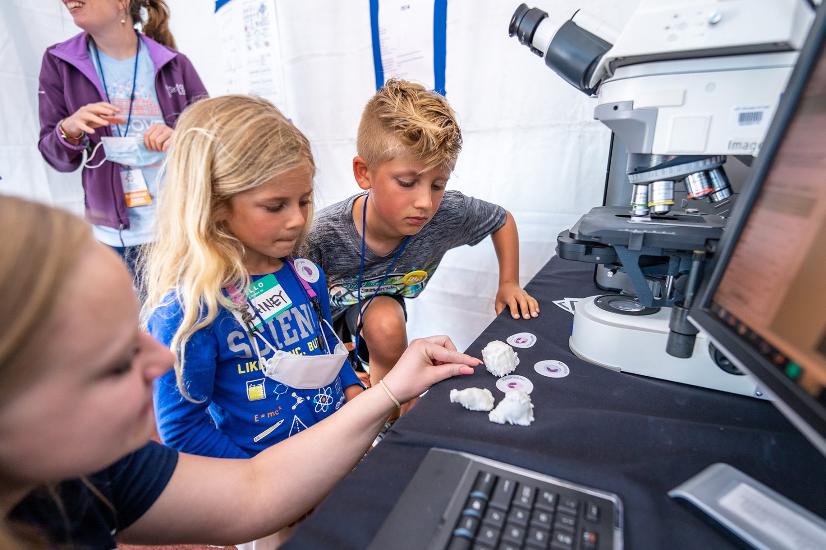 two children look at items on a table in front of a microscope