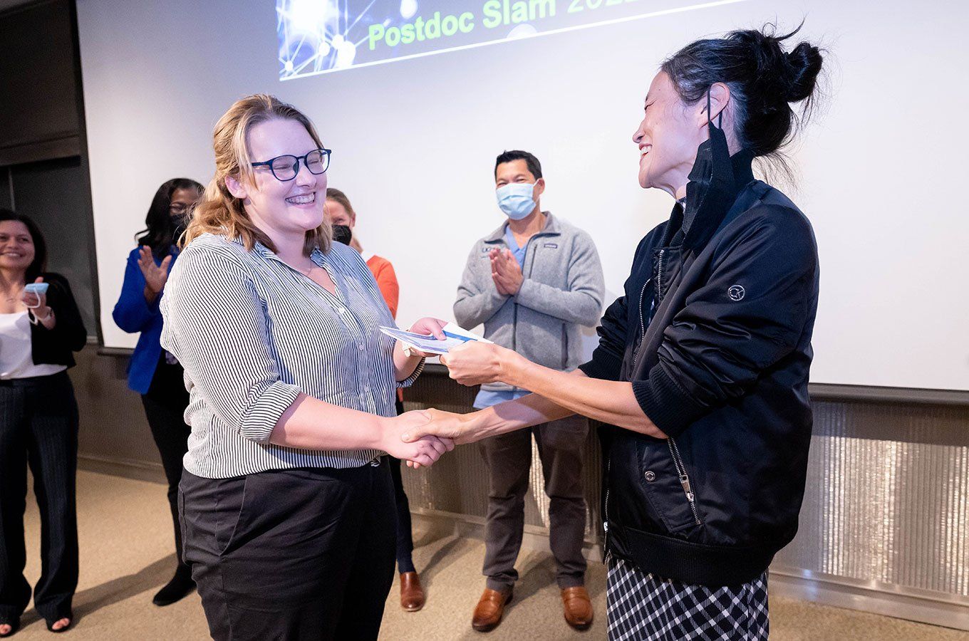Postdoctoral student Sophie Huddart shakes the hand of Mina Kim while accepting a third place award onstage
