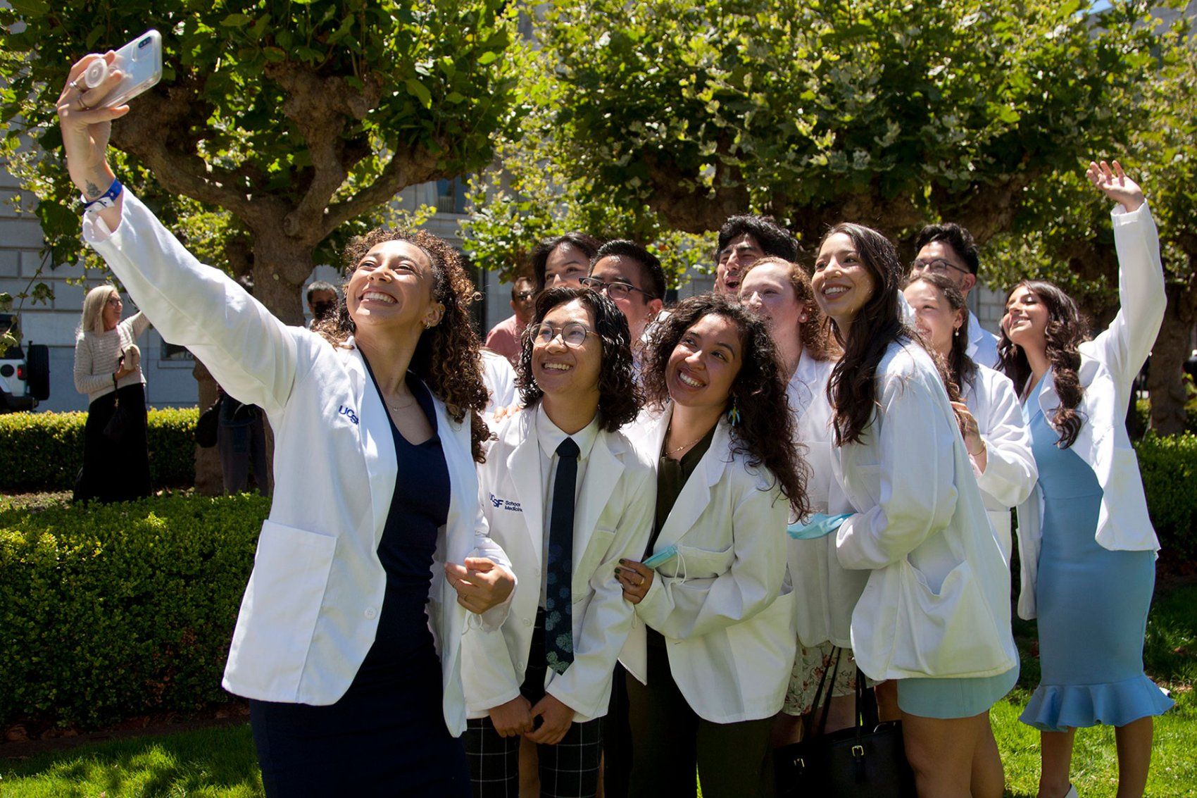 a group of medical students in white coats take a selfie outdoors