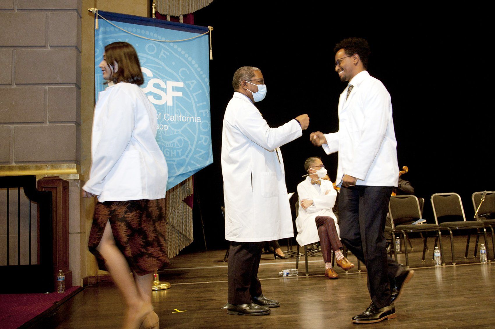 UCSF School of Medicine Dean Talmadge E. King Jr., MD, (center) fist bumps a new medical student in a white coat