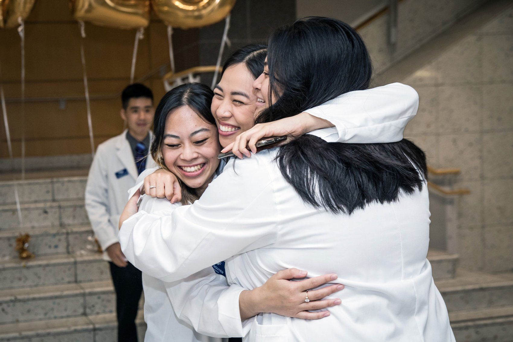 Three new pharmacy students in a white goat gather in a group hug