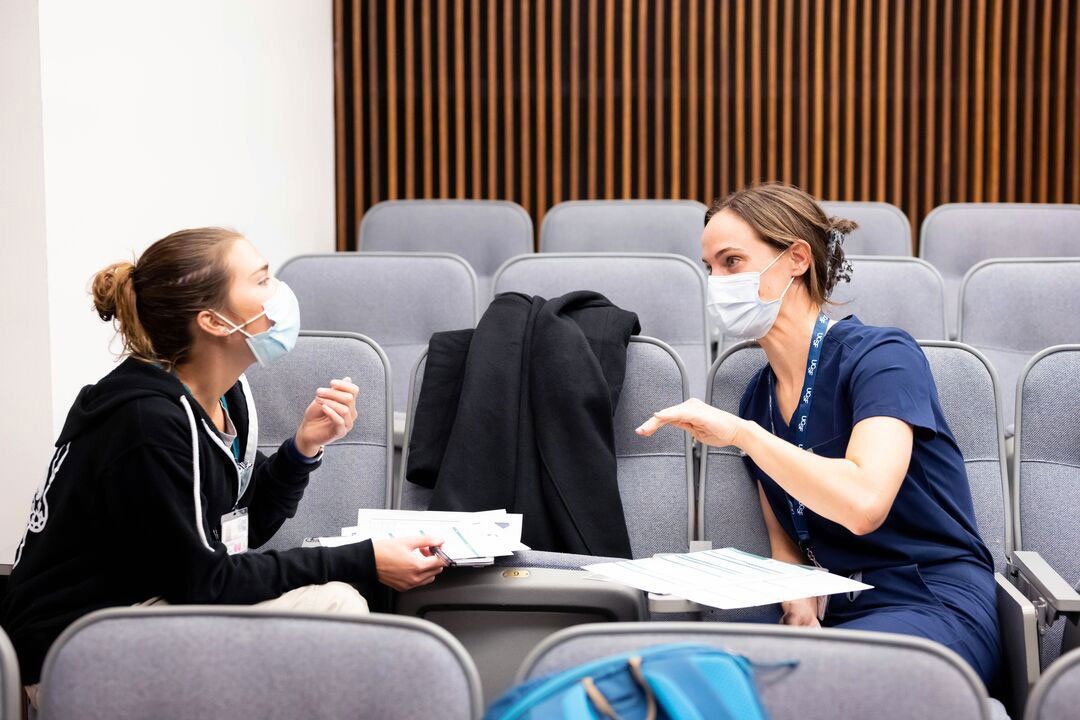 Two nursing master's students sit in an auditorium immersed in a discussion