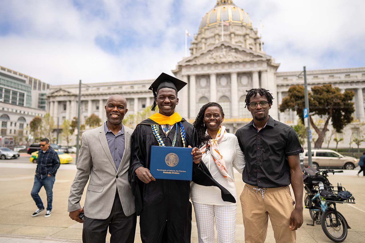 A new grad poses with his diploma and his family outside of San Francisco's City Hall