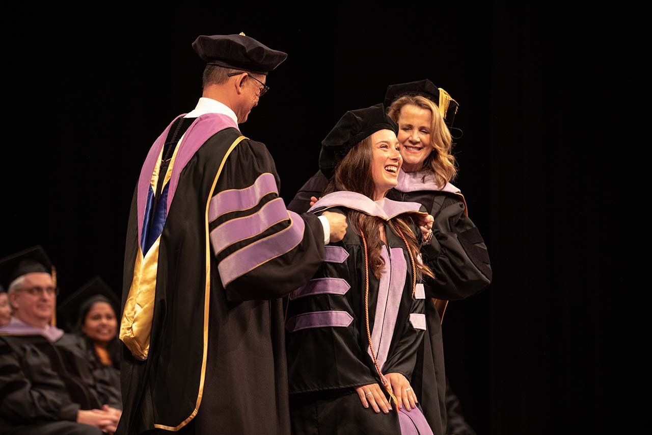 A new grad gives the crowd a huge smile while she's donned with a hood by two professors.