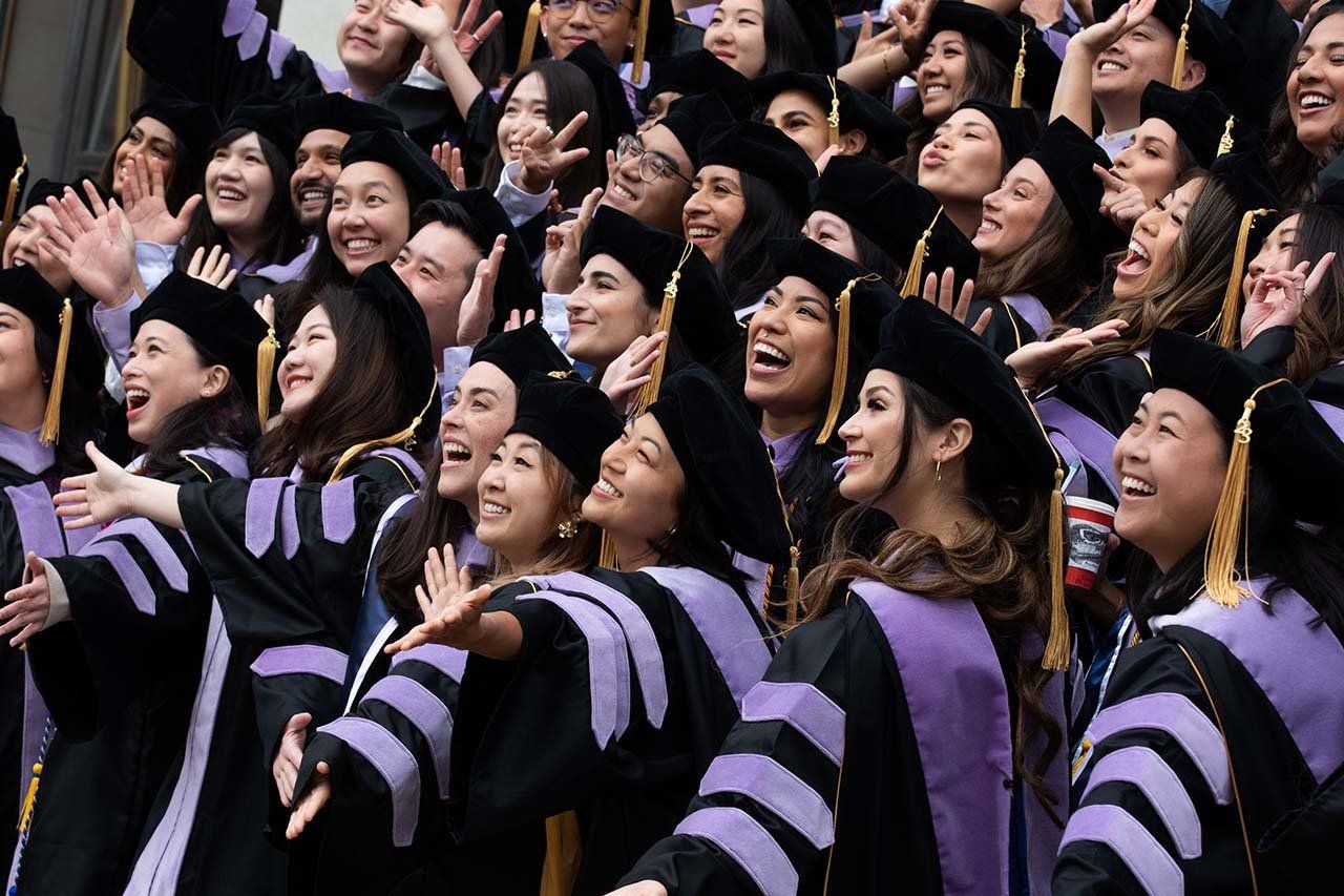 A huge crowd of new dentistry grads smile up for a photograph wearing black and purple gowns.