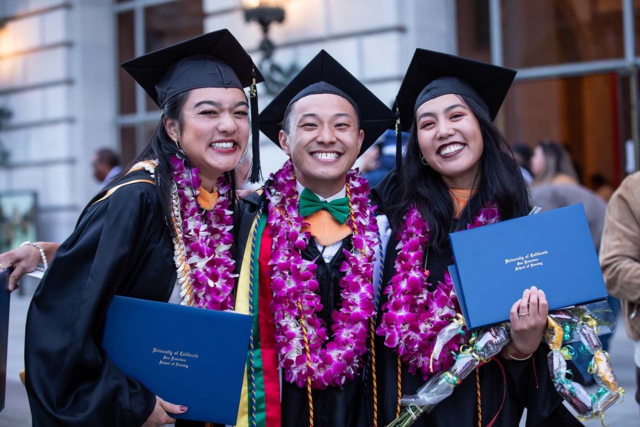 Three graduates wearing leis pose with their diplomas.
