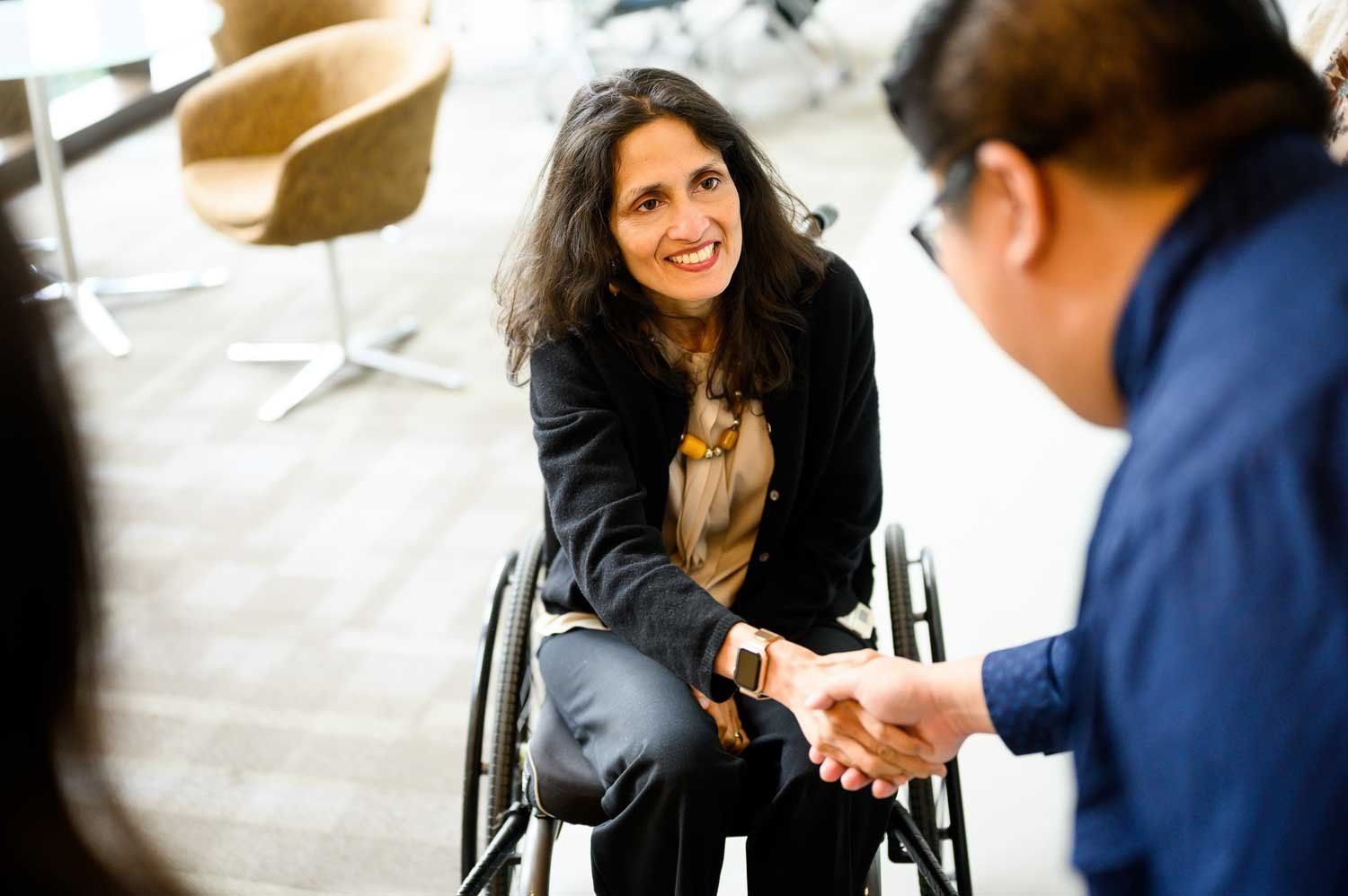 Janhavi Bonville sits in her wheelchair and smiles as she shakes hands with a colleague.