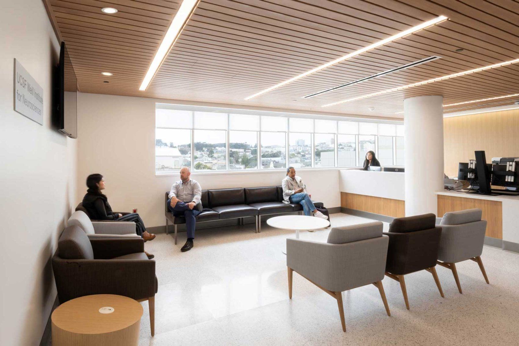 A comforting, light-filled reception area. A few people sit in modern grey and blue chairs.