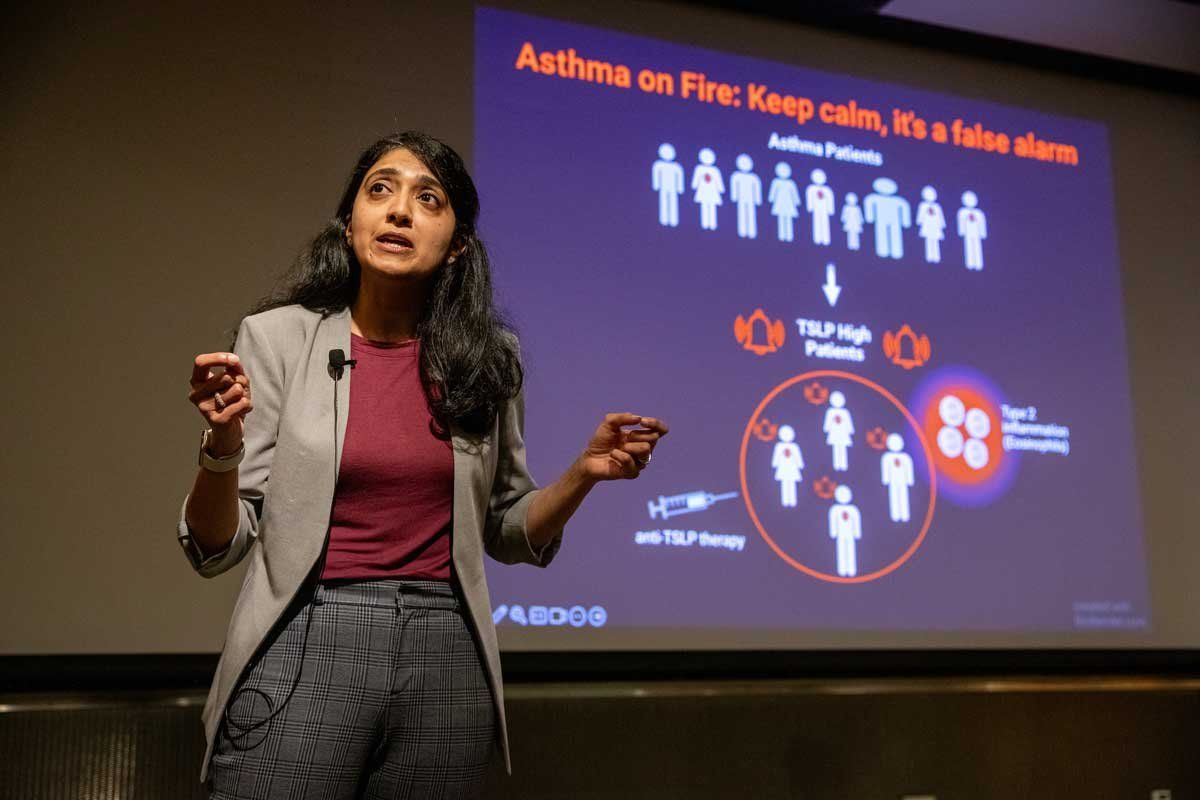 Kritika Khanna presents her talk onstage at Postdoc Slam 2023. Behind her is a screen that reads "Asthma on Fire: Keep Calm, It's a False Alarm."