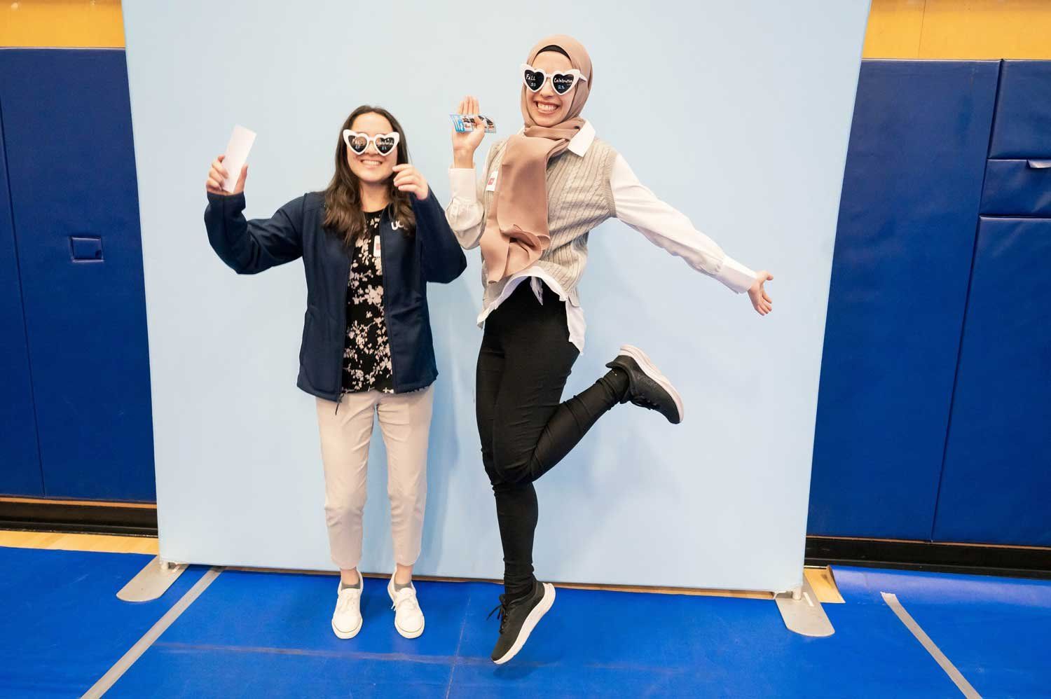 Two UCSF students wearing heart-shaped sunglasses pose for a fun photo in a gym at the 2023 Fall Celebration event.