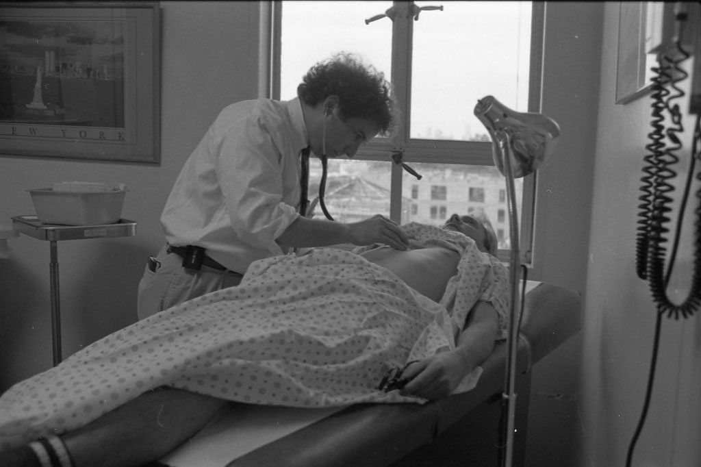 A greyscale photo of Mark Feinberg examining an AIDS patient on San Francisco General Hospital's Ward 86.