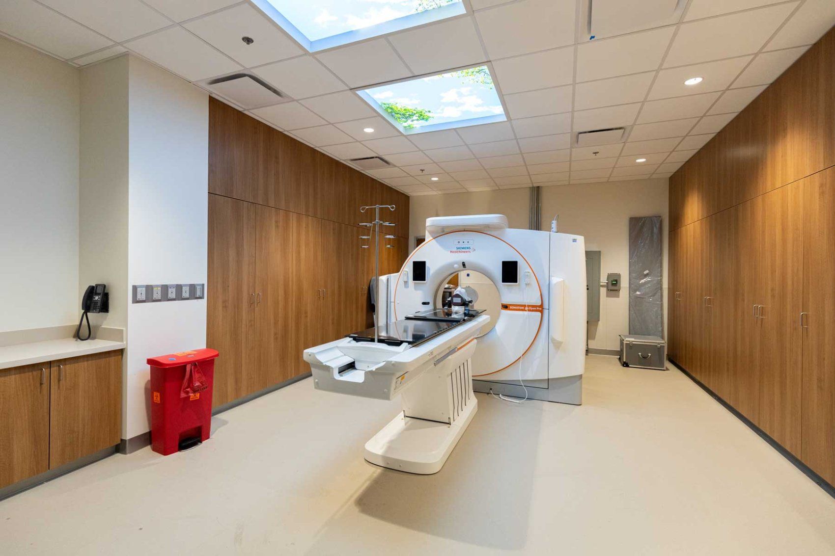 A CT scanner in an exam room with, warm, welcoming wood-paneled cabinets.