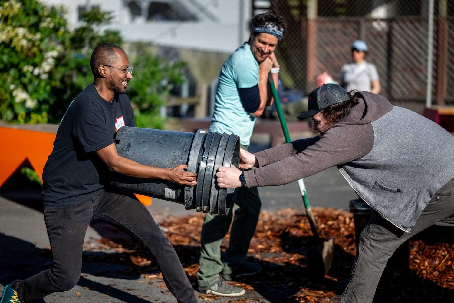 Two men smile as they try to pull stuck buckets together during a tree-planting event.