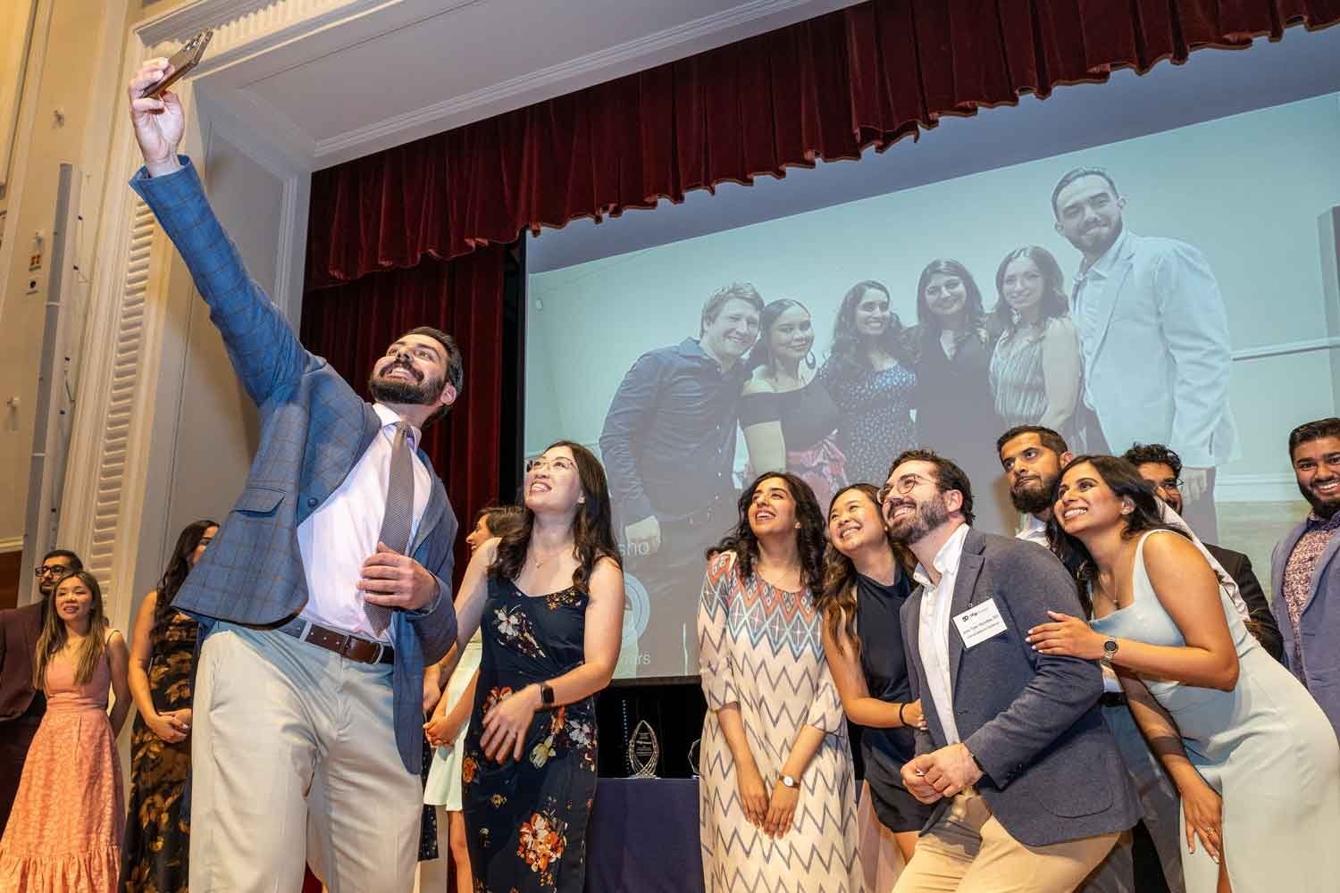 A group of graduates smile as they take a selfie on stage.