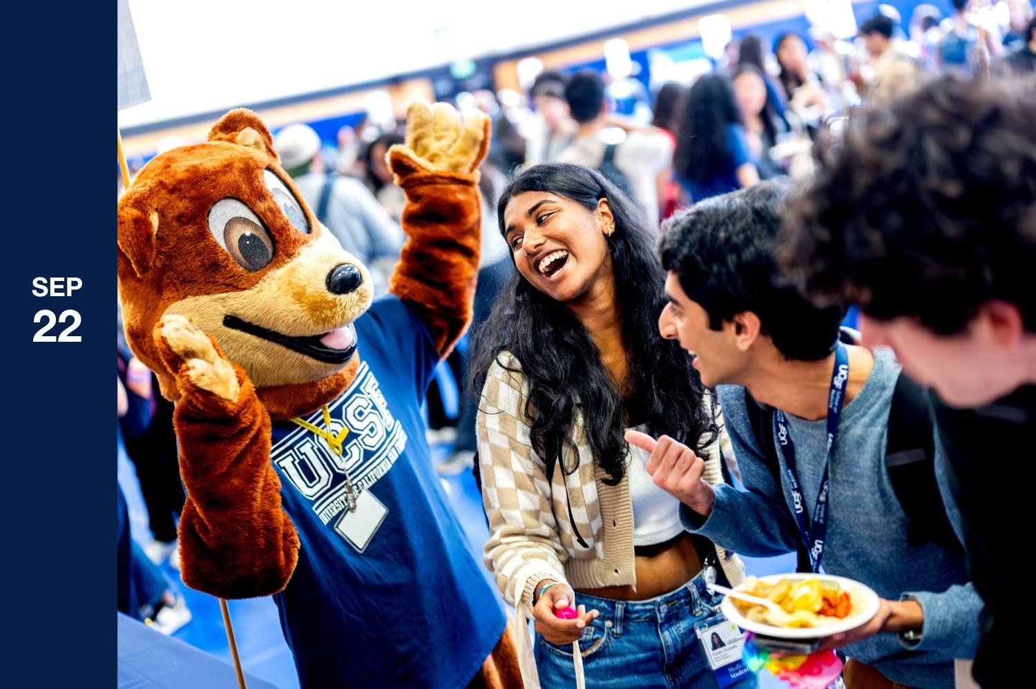 Suited bear laughs with students on campus.