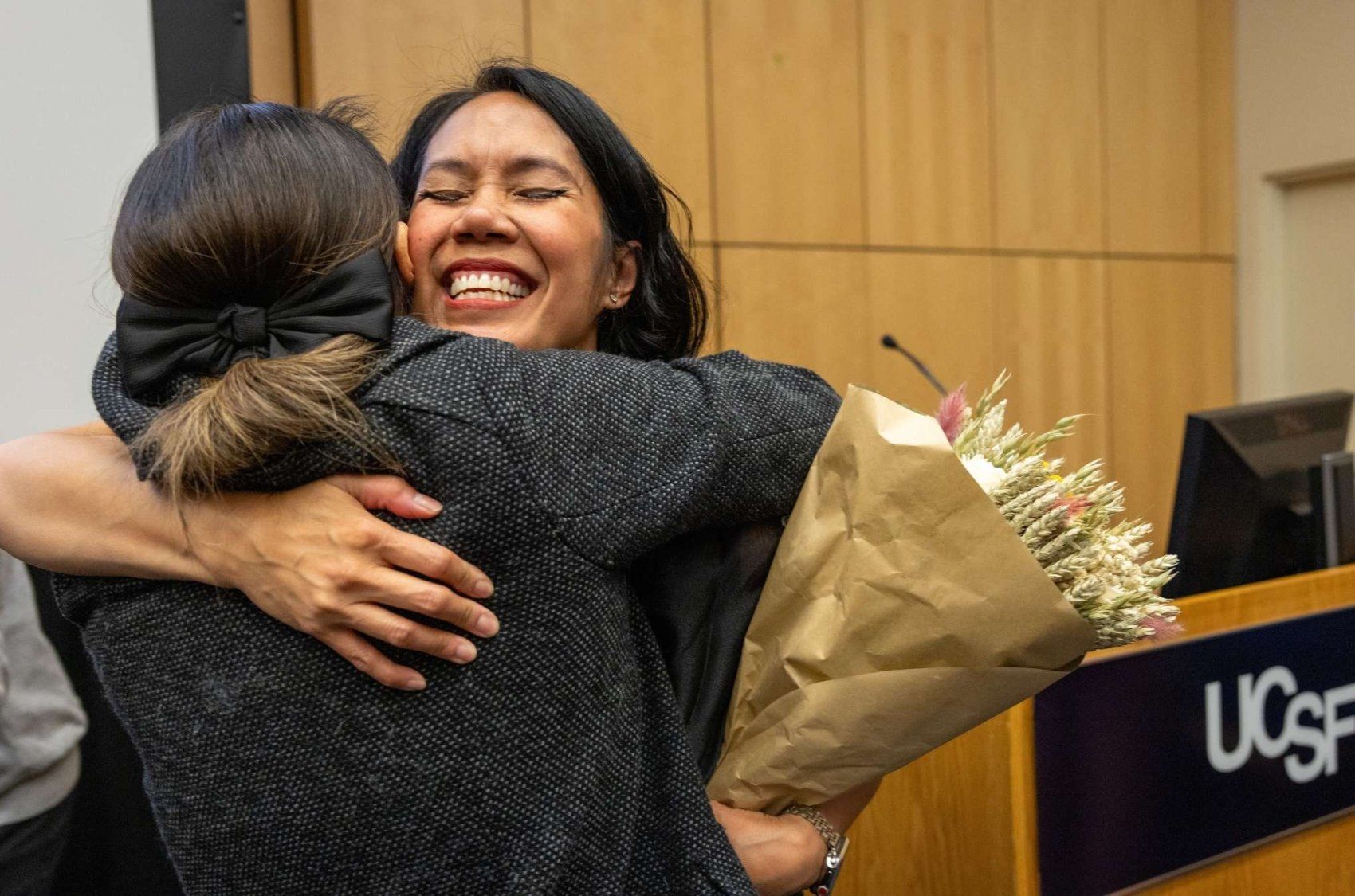Dr. Jennifer Cocohoba shares a warm embrace with an attendee holding a bouquet of flowers.