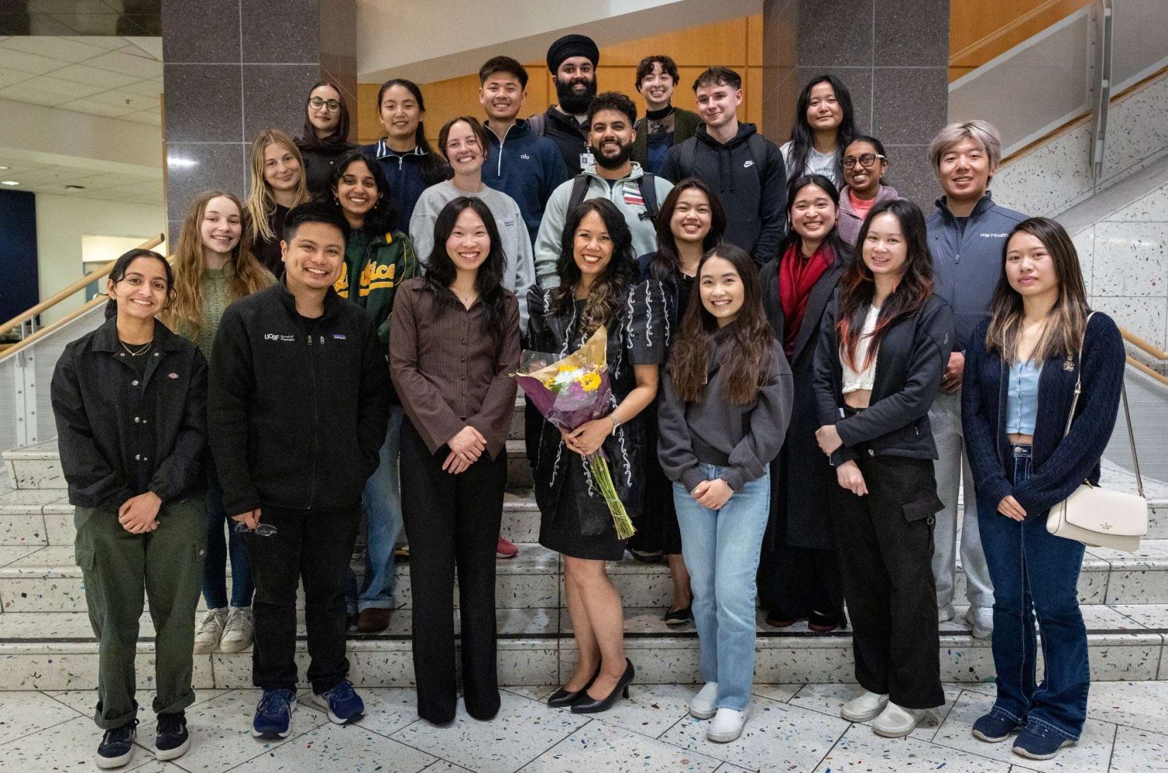 Dr. Jennifer Cocohoba smiles while posing with a large, diverse group of family members, faculty colleagues, and students.