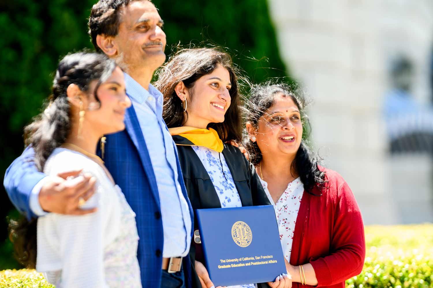 A graduate and her family smile as they pose together for a photo.
