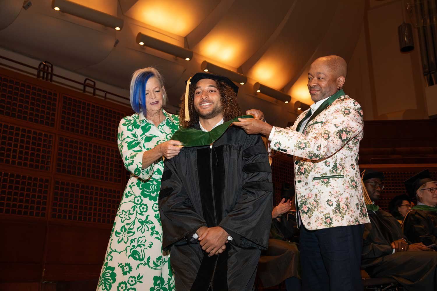 School of Medicine graduate Kamden Gray on stage with parents as he is ceremonially hooded.